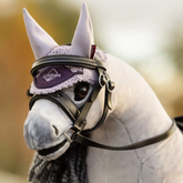 Close-up of a horse wearing a bridle with a visible brand logo against a blurred natural background